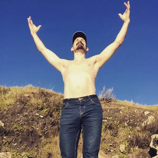 Jes with arms raised to the sky on a hillside